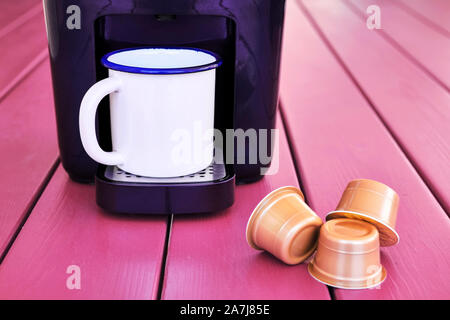 Espresso Cappuccino Maschine, Kapseln und ein Vintage Tasse auf einem rosa Holztisch. Morgen kapsel/Vorbereitung. Stockfoto