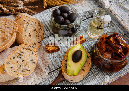 Gesunder Roggen Vollkornbrot mit Oliven, Avocado und getrocknete Tomaten auf die Tabelle, in der sich eine hölzerne Bauer. Hausgemachte Kuchen. Traditionelle italienische Küche. Stockfoto