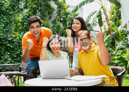 Happy Family älteren Eltern und erwachsener Sohn und Schwiegertochter mit Laptop Hände Faust Sieg feiern im Garten. Stockfoto