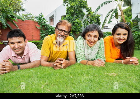 Happy Family älteren Eltern und erwachsene Sohn mit Schwiegertochter liegen auf Gras und Entspannen im Garten Ihres Hauses Stockfoto