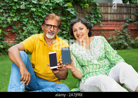 Gerne älteres Paar-auf-Gras und Übersicht Handy-in-park Stockfoto