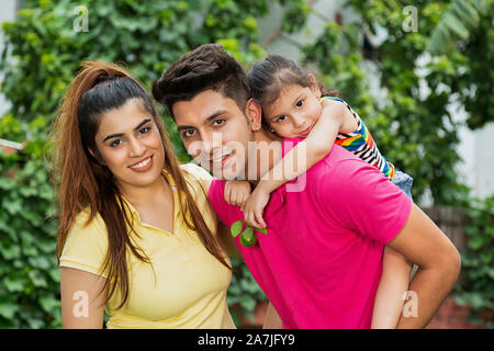 Glückliche junge Familie Mama, die seine kleine Tochter auf - Huckepack mit Mama im Garten Stockfoto