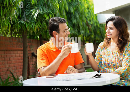 Glückliches Ehepaar sitzt am Tisch Trinken von Tee oder Kaffee und Reden - Hof - ihr Haus in Morgen Stockfoto