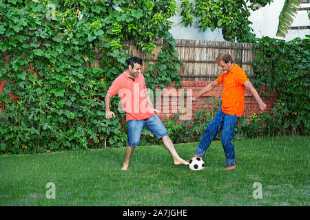 Gerne indische Familie ältere Vater und Sohn spielen Fußball Spiel in Regen In - Garten - Ihr Zuhause Stockfoto