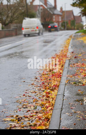 Blätter auf dem Bürgersteig und Straße, die im Herbst nach starken Winden und schwere Regenfälle mit Durchgangsverkehr gefallen sind. Dorset England UK GB Stockfoto