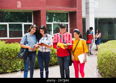 Vier junge Studenten Freunde lesen Buch zusammen gehen In-Outside Campus Stockfoto