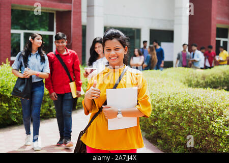 Portrait von Jugendmädchen Student Zeige Thumbs-up mit Mitschülern - Hintergrund At-Campus Stockfoto