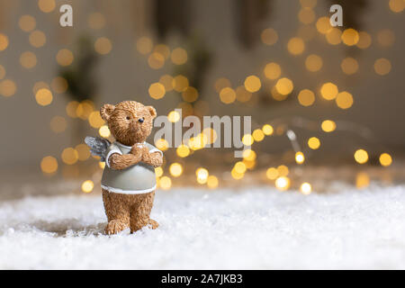 Dekorative Figuren aus einem Thema Weihnachten. Figurine eines süßen Bär mit Angel Wings. Festliches Dekor, warme Bokeh leuchtet. Stockfoto