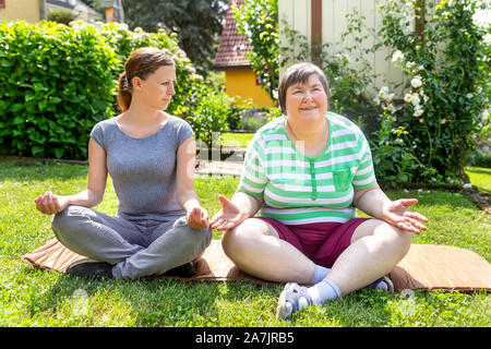 Zwei Frauen, eine von ihnen ein Fitness oder Yoga Trainer sind, tun etwas Yoga oder Entspannungsübungen, auf Frau ist geistig Behinderte. Stockfoto