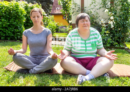 Zwei Frauen, eine von ihnen ein Fitness oder Yoga Trainer sind, tun etwas Yoga oder Entspannungsübungen, auf Frau ist geistig Behinderte. Stockfoto