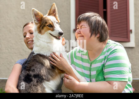 Geistig behinderte Frau vor einem Haus hält ihren Hund, Freundin oder Trainer neben Stockfoto