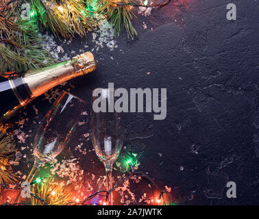 Bild der Zweige der Tanne,, brennen Girlanden, Champagner Flaschen, zwei Glas Wein auf schwarzem Hintergrund, Platz für Text Stockfoto