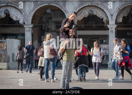 Ein glückliches Paar Blick auf Handy Foto in Piazza San Marco in Venedig, Italien. Die Frau ist auf den Schultern des Mannes sitzt. Stockfoto