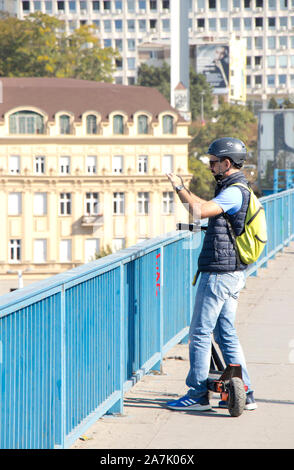 Belgrad, Serbien - Oktober 16, 2019: Ein tourist Mann Sightseeing beim Reiten eines elektrischen scooter auf Stadt Straße Brücke Bürgersteig Stockfoto