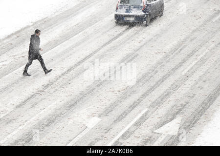 Belgrad, Serbien - Januar 26, 2019: Ein Mann über die Straße außerhalb der Zebrastreifen während der schneesturm und einem fahrenden Auto, hohe Betrachtungswinkel Stockfoto