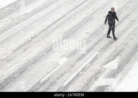 Belgrad, Serbien - Januar 26, 2019: Ein Mann über die Straße außerhalb der Zebrastreifen während der schneesturm und einem fahrenden Auto, hohe Betrachtungswinkel Stockfoto