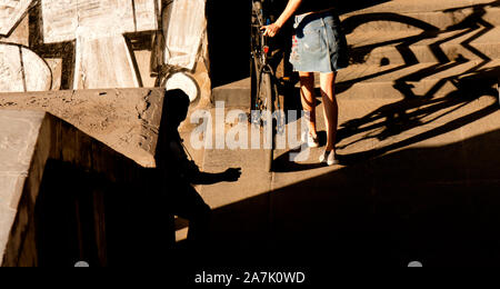 Ein junges Mädchen in kurzen Rock das Fahrrad schieben der öffentlichen Treppen in Sonne und Schatten, von hinten Stockfoto