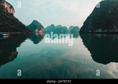 Klar Grün ember Gewässern spiegeln den hohen Kalkstein Inseln in Ha Long Bay, Vietnam bei einem schönen Sonnenuntergang mit Ruhe, ruhige See. UNESCO-Welterbe Stockfoto