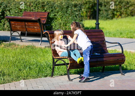 Ein kleines Mädchen ist die Anwendung aqua Make-up im Gesicht ein 5 Jahre alter Junge, sitzen auf einer Bank in einem Park. Stockfoto