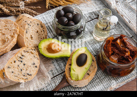 Gesundes Roggenvollkornbrot mit Oliven, Avocado und sonnengetrockneten Tomaten auf einem Holzbäuertisch. Hausgemachter Kuchen. Traditionelle italienische Küche Stockfoto
