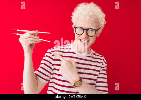 Junge albino blonde Mann mit Stäbchen über isoliert weißer Hintergrund stehend sehr glücklich zeigte mit Hand und Finger Stockfoto