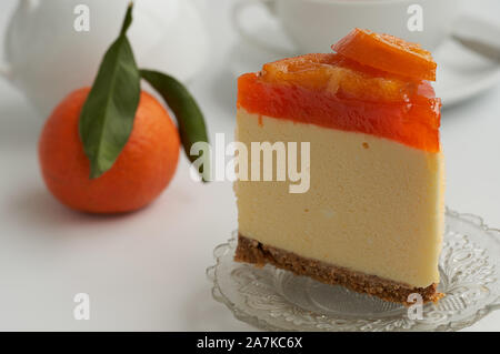 Close-up ein Stück kandierten Orangen Kuchen mit einer frischen Orange, eine Teekanne und eine Tasse Tee in Soft-Schwerpunkt im Hintergrund Stockfoto
