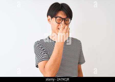 Chinesischer Mann mit Brille und Marine gestreiftes T-Shirt stehend über isoliert weißer Hintergrund riechen etwas stinkig und ekelhaft, unerträgliche KMU Stockfoto