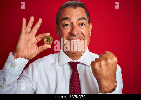 Gut aussehender Mann mittleren Alters holding Bitcoin stehend über isolierten roten Hintergrund schreien stolz und feiern Sieg und Erfolg sehr aufgeregt, cheeri Stockfoto