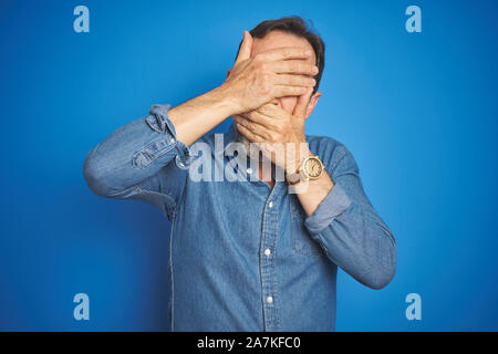 Stattliche mittleren Alters älterer Mann mit dem grauen Haar über isolierte blauen Hintergrund für Augen und Mund mit den Händen, überrascht und schockiert. Ausblenden von Emotion Stockfoto