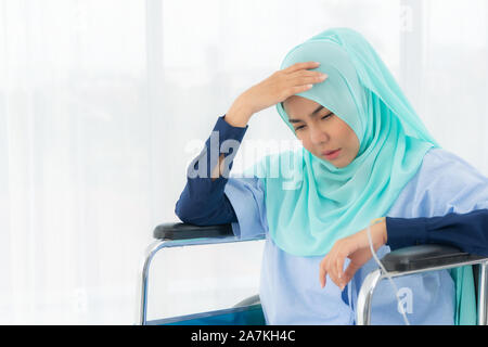 Muslimische Frau tragen eine grüne Kopfbedeckung Sitzen im Rollstuhl, wie Sie hat Kopfschmerzen. Stockfoto