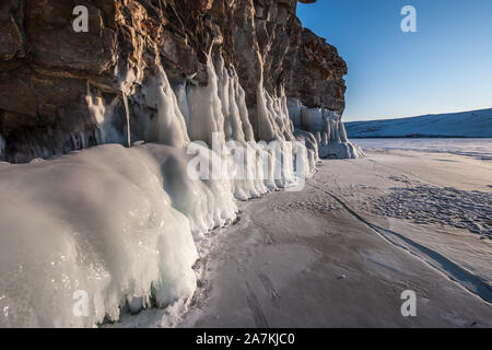 Eine dicke Schicht von Eis auf einem Felsen von der Sonne beleuchtet. Der See ist mit Eis und Schnee bedeckt. Stockfoto