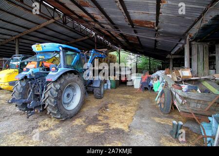 Norden, England - 29.August 2018: Alte heruntergekommene Farm Barn oder Schuppen, mit einigen modernen landwirtschaftliche Fahrzeuge unter anderem alte Traktoren, Karren und Junk Stockfoto