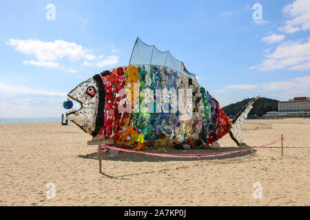 BUSAN, SÜDKOREA - 16. OKTOBER 2019: Fisch Installer aus dem Schutthaufen des leeren Plastikflaschen und Waschmittel Container am Strand Haeundae erstellt Stockfoto