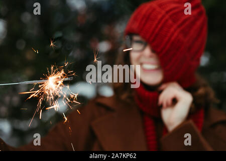 Junge schöne Frau in gestrickt, Red Hat und Schal im Park mit Bengal Licht, Sparkler. Konzept Feier, Weihnachten. Winter Stockfoto