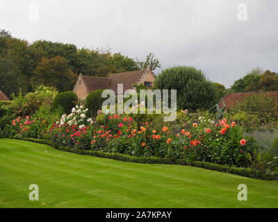 Schöne gebogene Anlage Grenze mit orange, pink und kirschrot Dahlien an chenies Manor Garden verpackt im Spätsommer; auch weiße Rosen, Formgehölze, Pavillon. Stockfoto