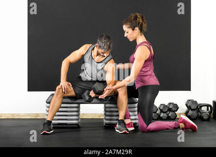 Weibliche Fitness Trainer helfen, ein Mann in einer Turnhalle locken mit einer hantel Gewicht seinen Bizeps in einem Gesundheit und Fitness Concept zu stärken zu tun Stockfoto