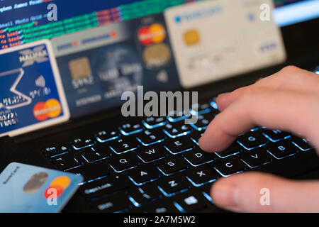 Eine Hand, die Eingabe über eine Tastatur mit Bildschirm und Kreditkarten im Hintergrund. Konzept: Betrug mit gestohlenen Kreditkarten online Zahlung zu machen Stockfoto