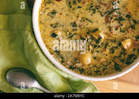 Eine große Schüssel mit Zuppa Toscana Suppe mit bright green Serviette und Löffel dargestellt. Toskanische Eintopf, italienische Küche. Stockfoto