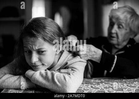 Kleines Mädchen Winces an der Tatsache, dass ihre Großmutter Zöpfe Haar. Stockfoto