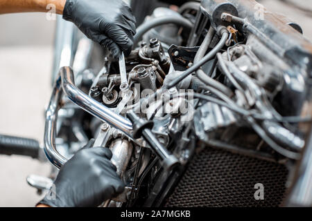 Arbeiter in Schutzhandschuhe Einstellung der Ventile von einer wunderschönen Oldtimer Motorrad an der Werkstatt, Nahaufnahme Stockfoto