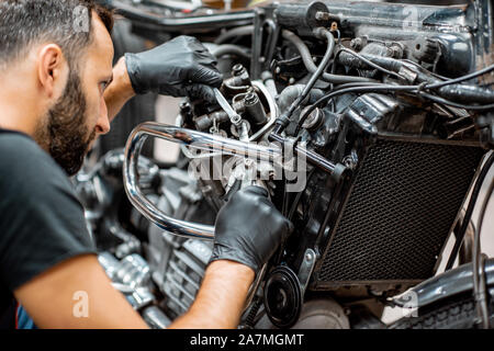 Schöner Mann in Arbeitskleidung Einstellung der Ventile von einer wunderschönen Oldtimer Motorrad in der Werkstatt Stockfoto