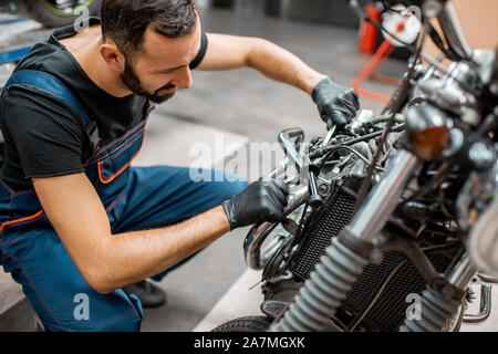 Schöner Mann in Arbeitskleidung Einstellung der Ventile von einer wunderschönen Oldtimer Motorrad in der Werkstatt Stockfoto