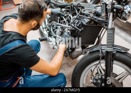 Schöner Mann in Arbeitskleidung Einstellung der Ventile von einer wunderschönen Oldtimer Motorrad in der Werkstatt Stockfoto