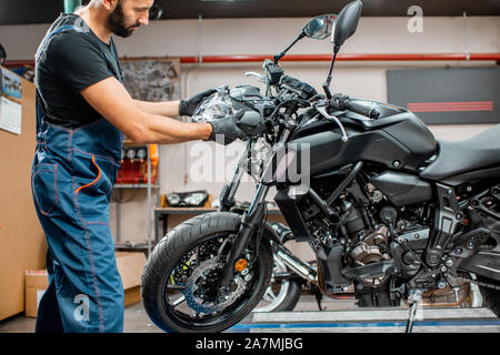 Stattliche Arbeiter in Overalls Entfernen des defekten Scheinwerfer, Instandsetzung mototrcycle nach dem Unfall in der Werkstatt Stockfoto