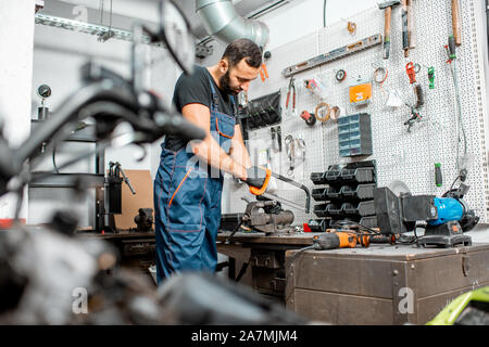 Handwerker in Latzhosen am Arbeitsplatz arbeiten mit vielen insrtuments am Workshop mit Motorrad auf den Vordergrund Stockfoto