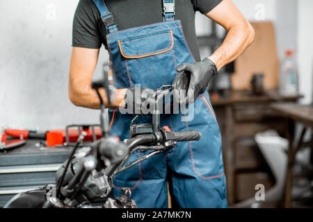 Mechaniker in Latzhosen Motorrad reparieren, Messen spiegel halter für Ersatz oder Tuning bei dem Workshop im Innenbereich Stockfoto