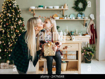 Portrait von Mutter und Tochter in der Vorfreude auf Weihnachten. Mama küsst sie Tochter und gibt ein Geschenk Stockfoto