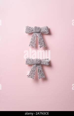 Urlaub Dekorationen Sammlung, zwei glänzenden silbernen Schleife auf rosa Hintergrund. Konzept für Weihnachten und Feiertage. Stockfoto