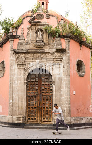 Ein Junge auf einem Skateboard übergibt die kleine barocke Kapelle von La Concepción Cuepopan auch als La Conchita oder die Kapelle der Toten in der Concepcion Platz von Mexiko-Stadt, Mexiko kennen. Stockfoto