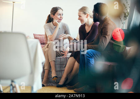 In voller Länge ansehen In der Gruppe der modernen jungen Menschen plaudern, während auf der gemütlichen Sofa bei Weihnachtsfeier sitzen, Platz kopieren Stockfoto